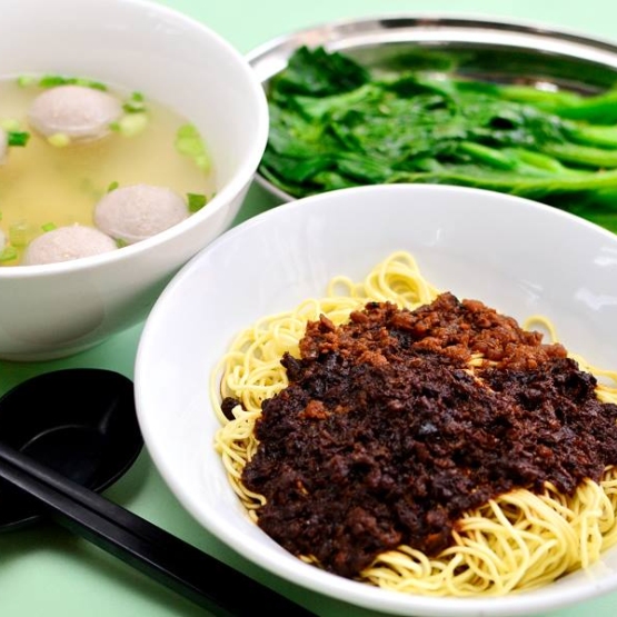 A bowl of noodles, beef ball soup and steam vegetables on a table